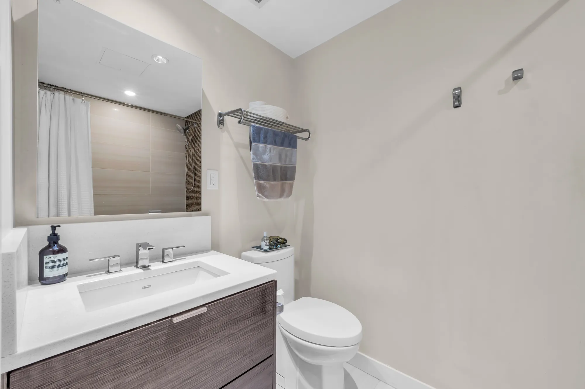 The bathroom: a floating wood vanity with a white counter, a tub with a curtain, a mirror, white tile