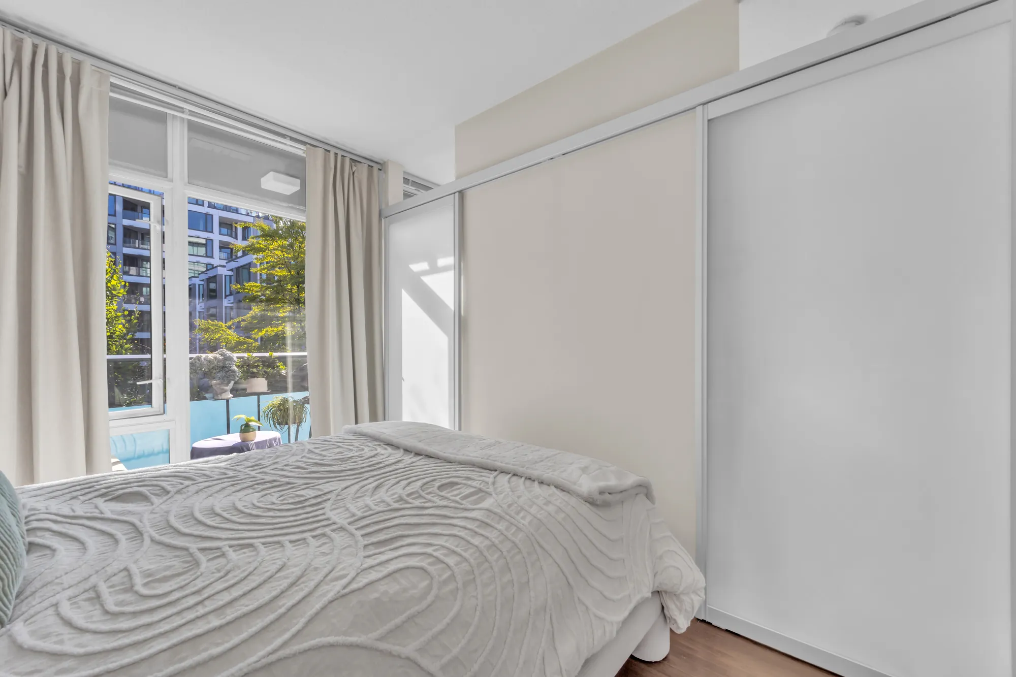 The bed and the window with its curtains, the sliding glass wall open on the right