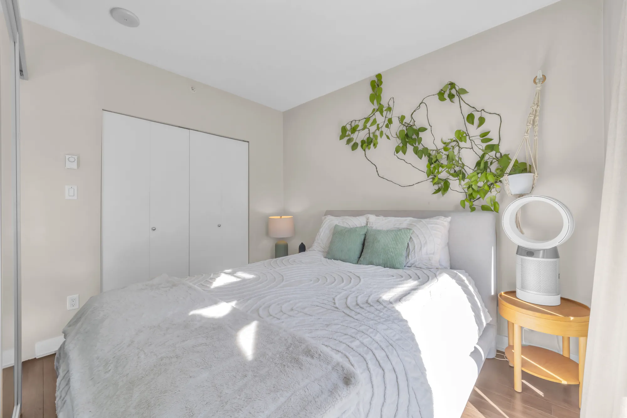 The bedroom toward its closet doors: the bed, a lamp, a fan, a plant on the wall