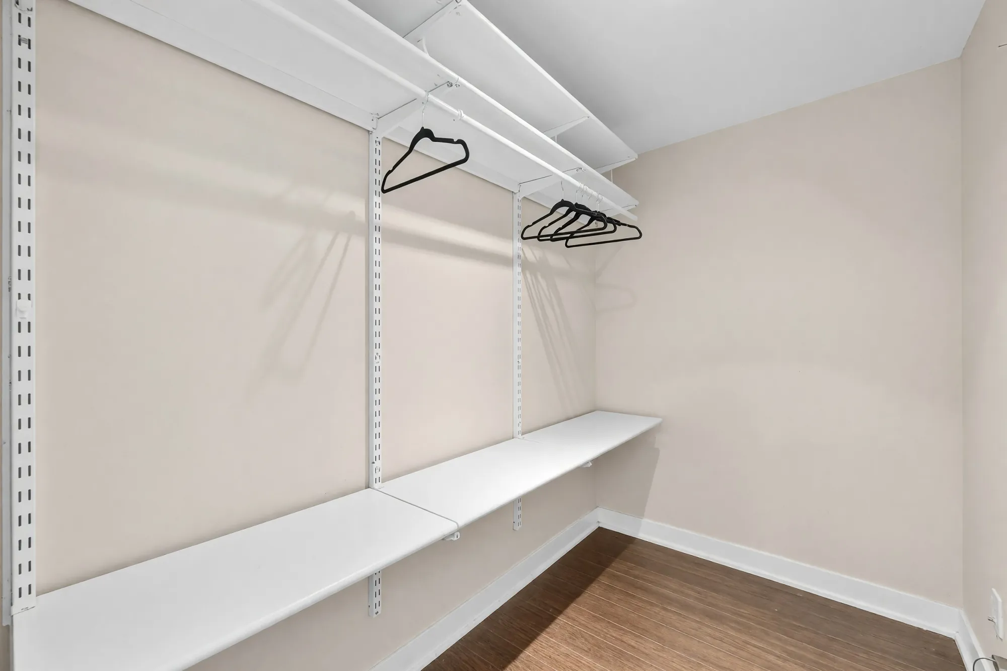 The closet shown empty: white rail shelving with hangers along one wall, laminate floor