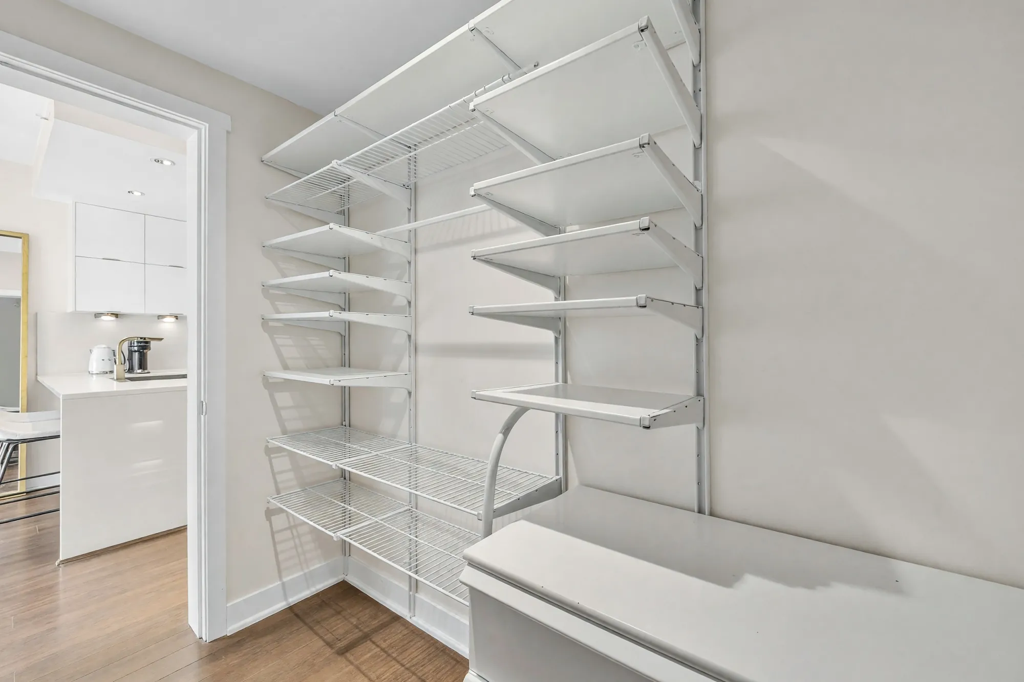 The den shown empty: wire shelving on one wall, a white bench, the door open to the kitchen