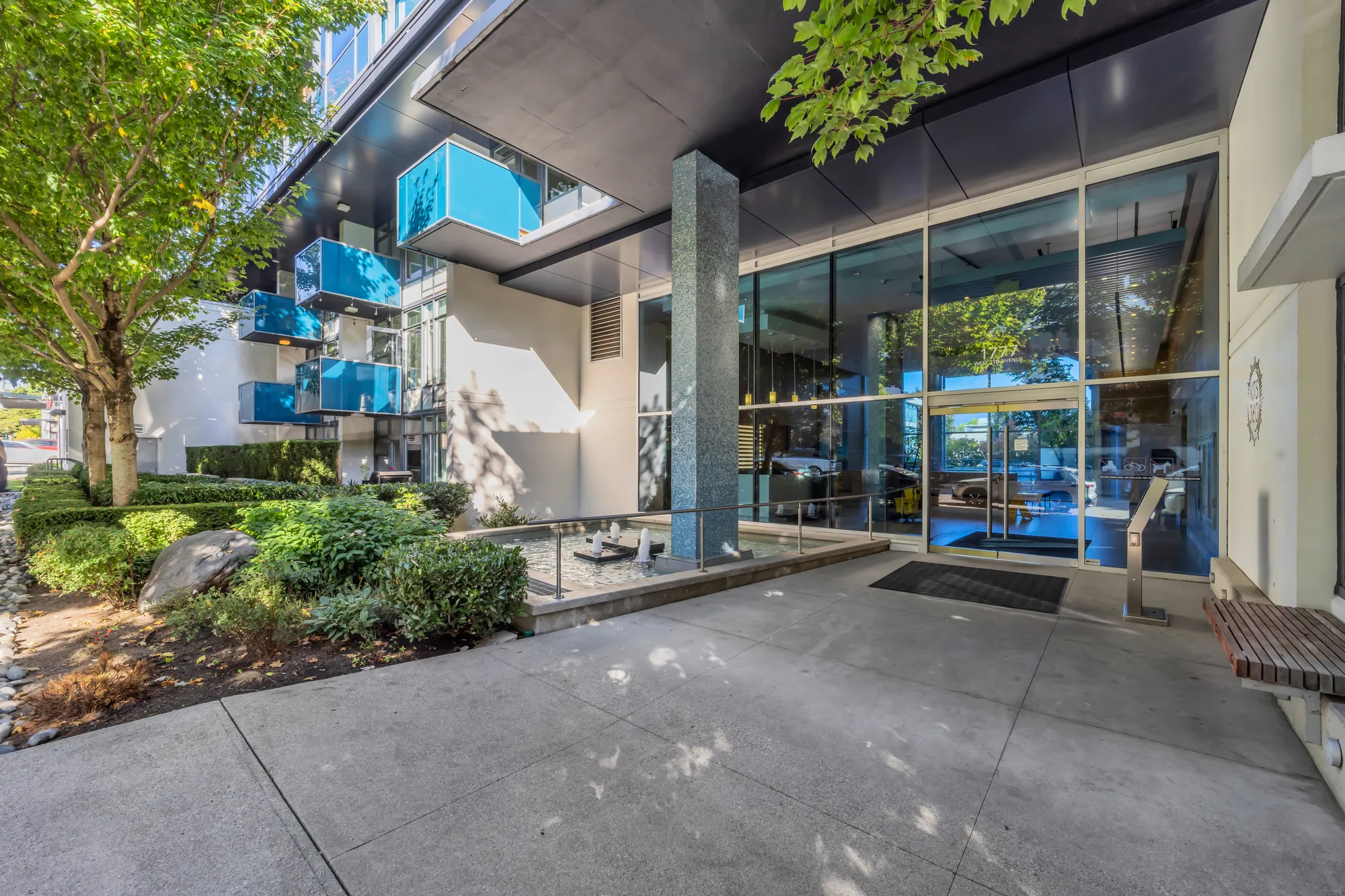 The entrance on 7th Avenue: glass doors under a canopy on stone columns, trees along the sidewalk