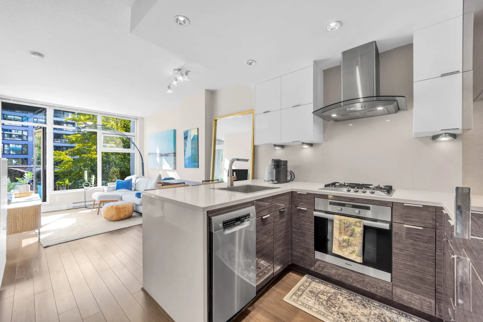 The kitchen: high-gloss white uppers, wood-grain lowers, a stainless hood, a gas cooktop, the peninsula counter and the living room beyond
