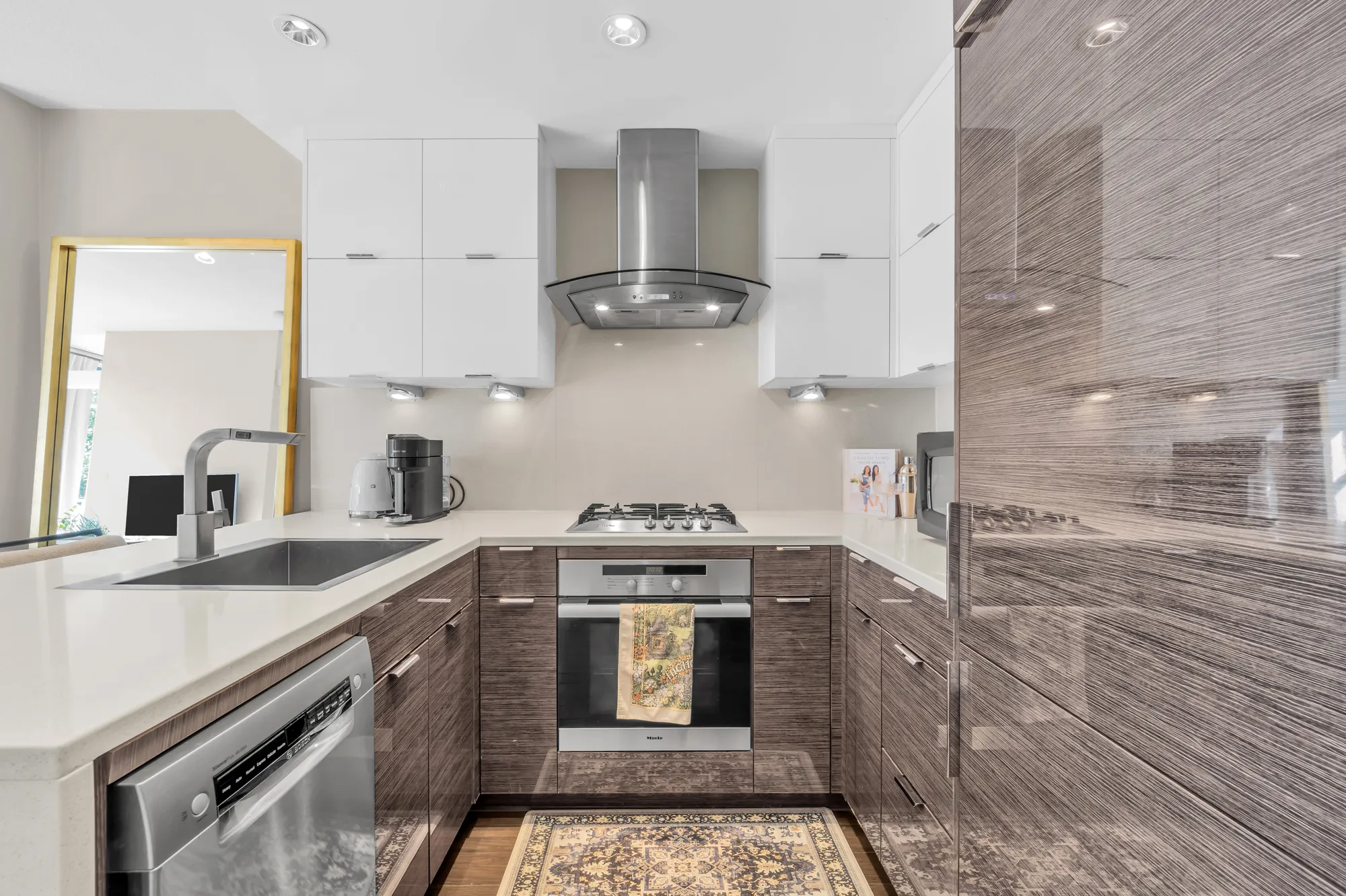 The kitchen's U of counters: the sink, the dishwasher, the gas cooktop under its hood, the wall oven, a mirror on the wall