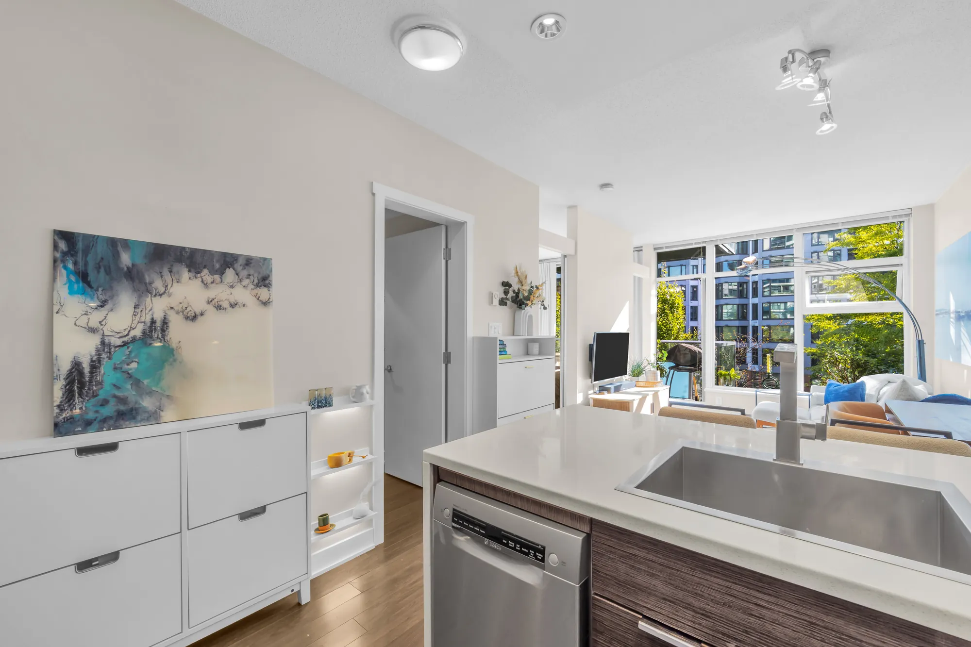 The kitchen's sink in the peninsula counter, a painting, the door to the den and the living room beyond