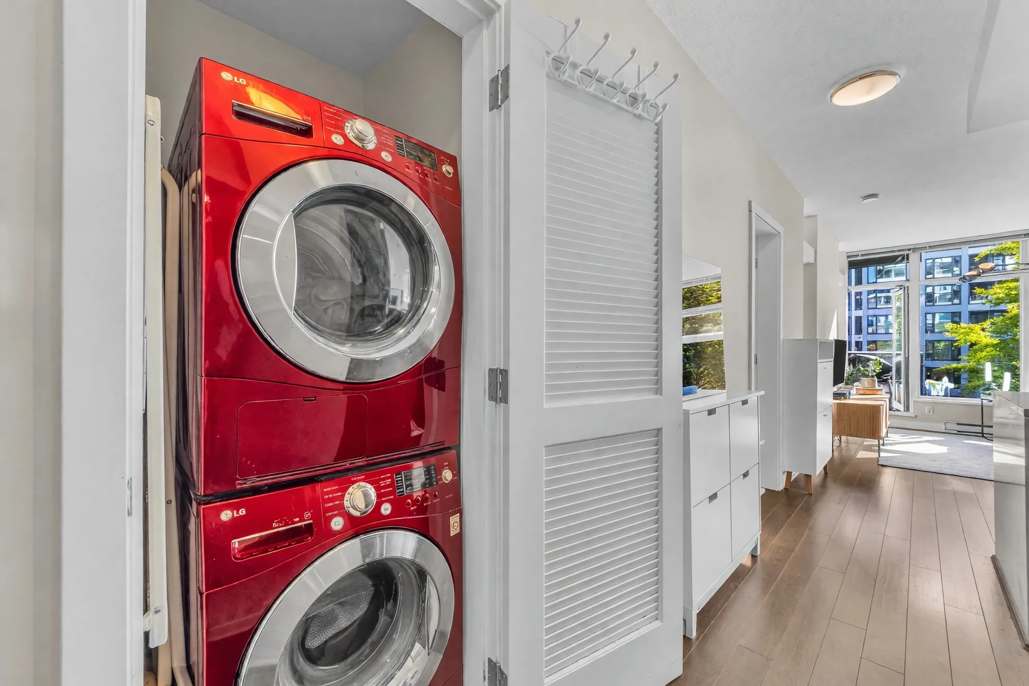 The laundry closet by the door: a stacked red washer and dryer behind a louvred door, the hall to the living room beyond