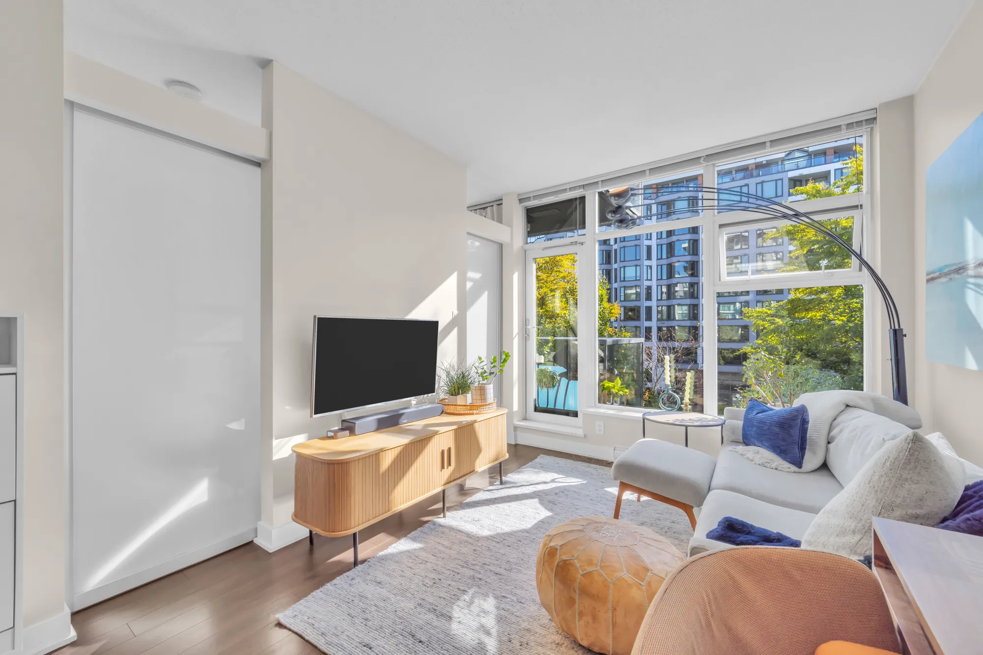 The television console under the window, the tan chair, the sliding glass wall of the bedroom on the left
