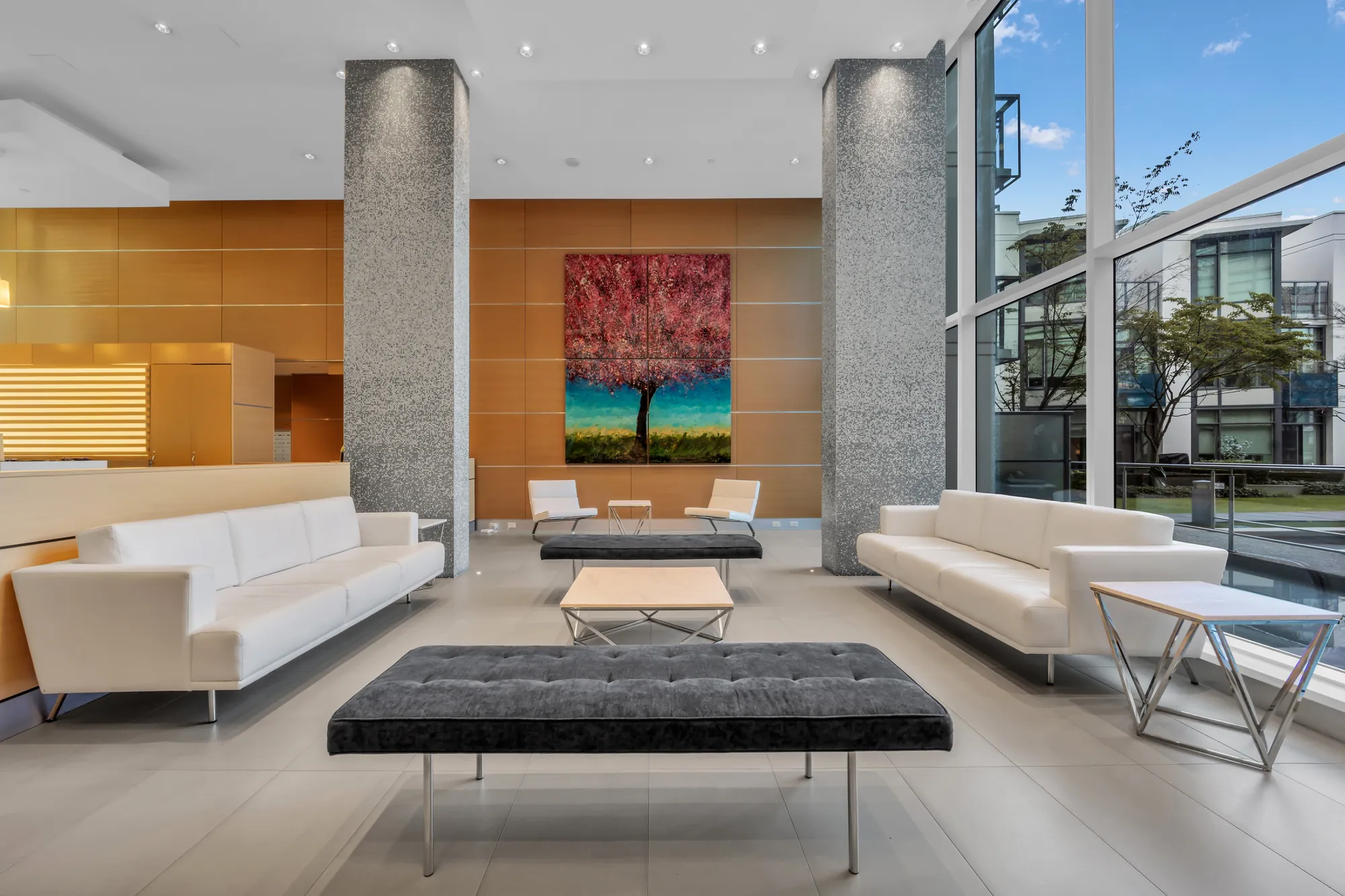 The lobby: white leather sofas and a black bench under a painting of a red tree, wood panelling, a grey stone column