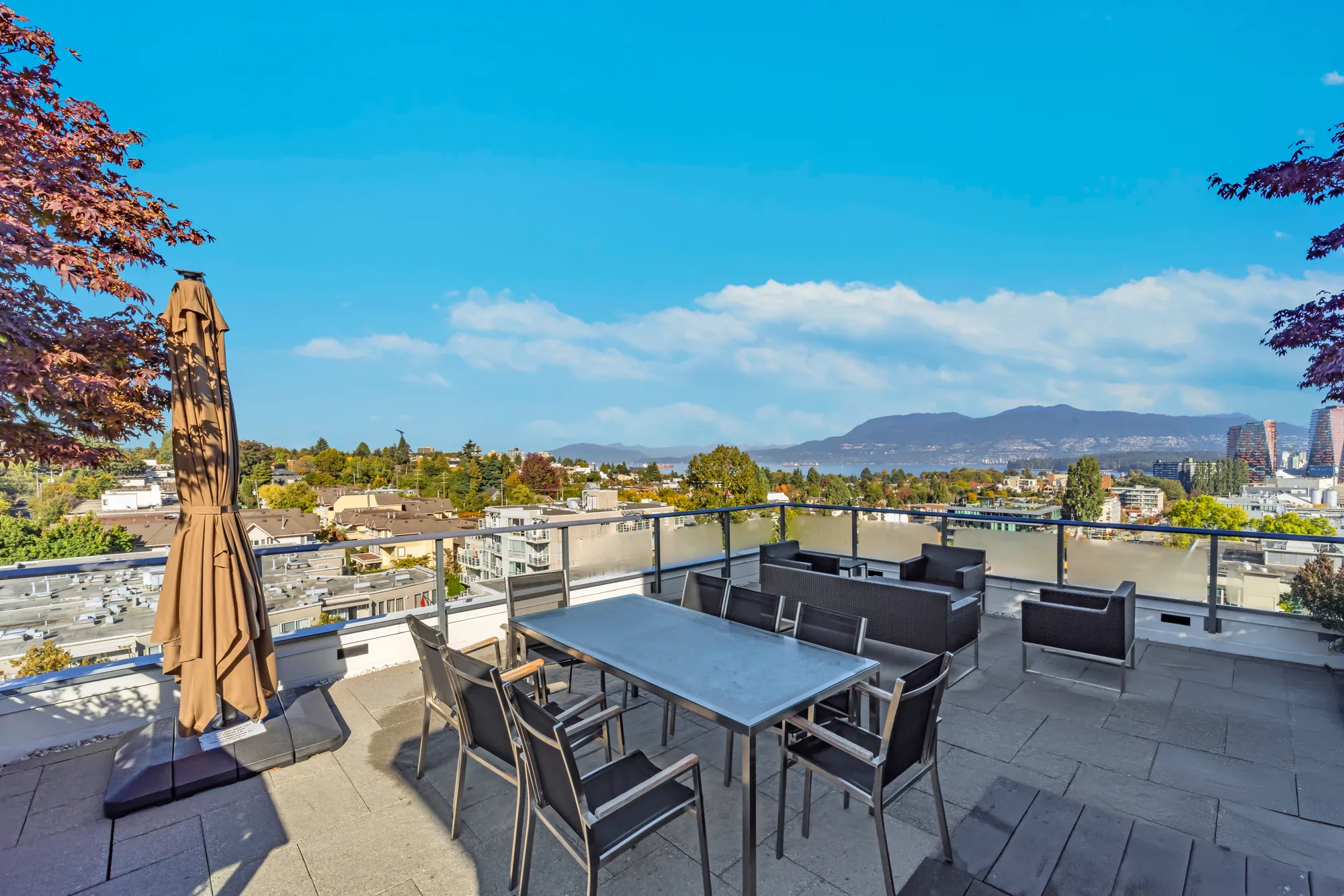 The rooftop terrace: a long dining table and chairs under an umbrella, the mountains on the skyline