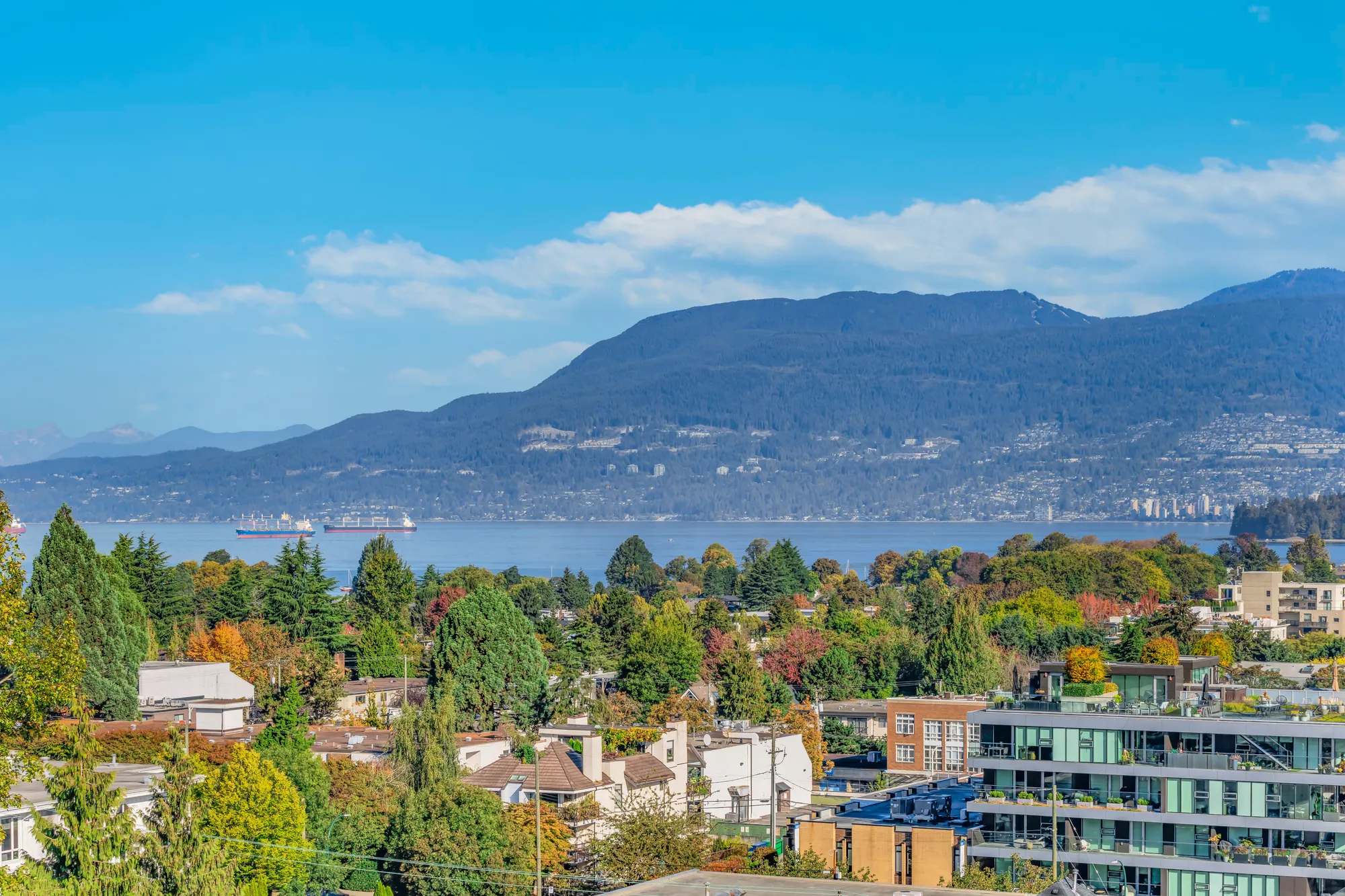 From the rooftop terrace: the rooftops of Kitsilano, English Bay and the North Shore mountains under a blue sky